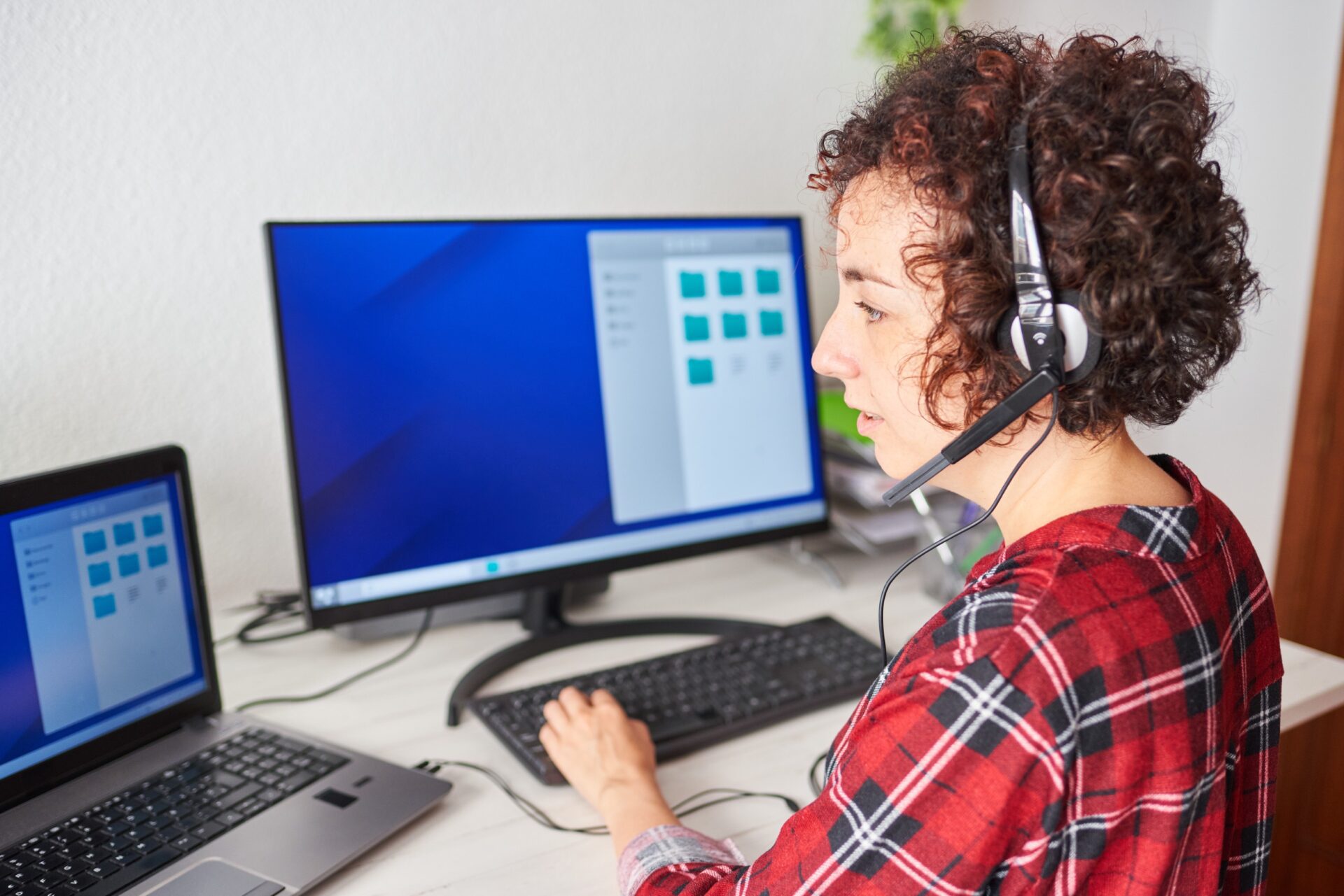 A young woman in a headset works at a computer at home.<br />
